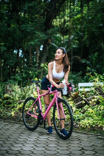 Portrait der jungen schönen Frau mit rosafarbenem Fahrrad im Park. Actractive gesunde Frau.