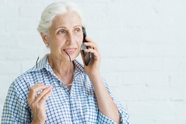 Portrait der lächelnden älteren jungen Frau, die am Handy spricht