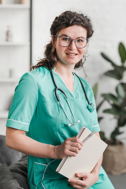 Portrait der lächelnden jungen weiblichen Krankenschwester, die auf Sofa sitzt