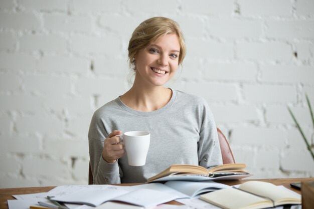 Portrait der lächelnden Student Mädchen am Schreibtisch, Becher in der Hand