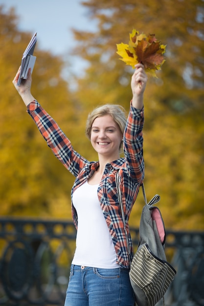 Portrait der lächelnden weiblichen jungen Studenten im Freien mit gelben Blättern