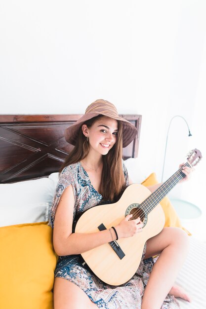 Portrait einer glücklichen Jugendlichen, die auf dem Bett spielt Gitarre sitzt