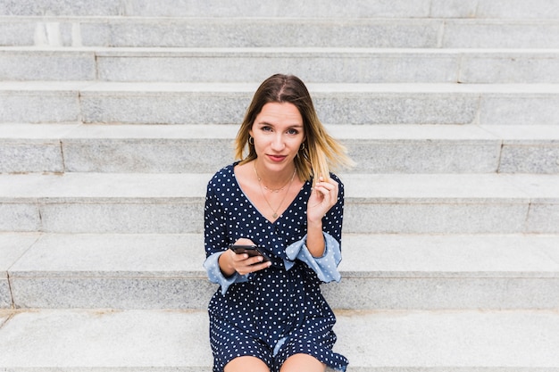 Portrait einer jungen Frau, die auf Treppenhaus mit Handy sitzt