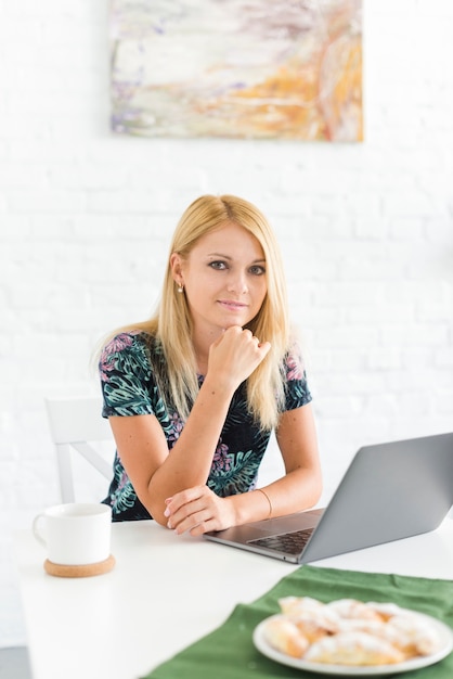 Portrait einer jungen Frau mit dem Laptop, der Kamera betrachtet