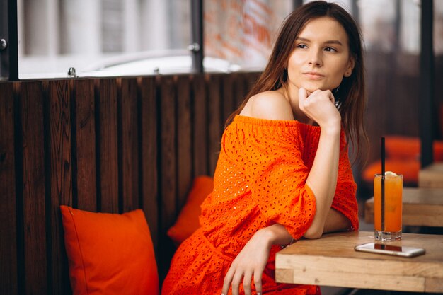 Portrait einer jungen Frau mit Telefon in einem trinkenden Saft des Cafés