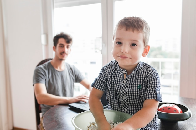 Portrait eines Jungen mit dem Popcorn, das auf Tabelle sitzt