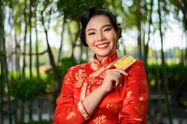Portrait schöne asiatische Frau in einer chinesischen Cheongsam-Pose mit Kreditkarte auf Bambuswald