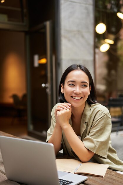 Portrait von asiatischen Mädchen arbeitet im Freien im Café sitzt mit Laptop-Studien lächelt glücklich