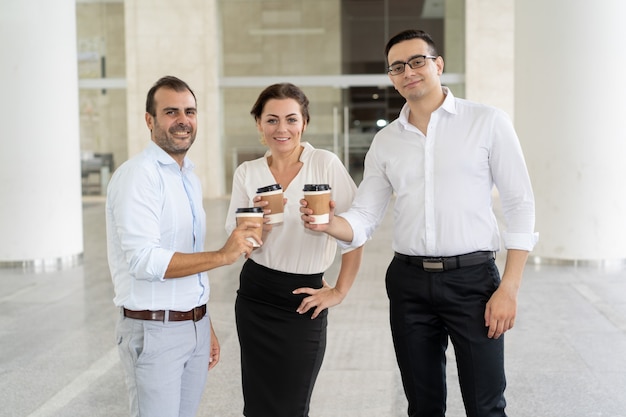 Portrait von drei lächelnden Kollegen, die mit Kaffeetassen stehen