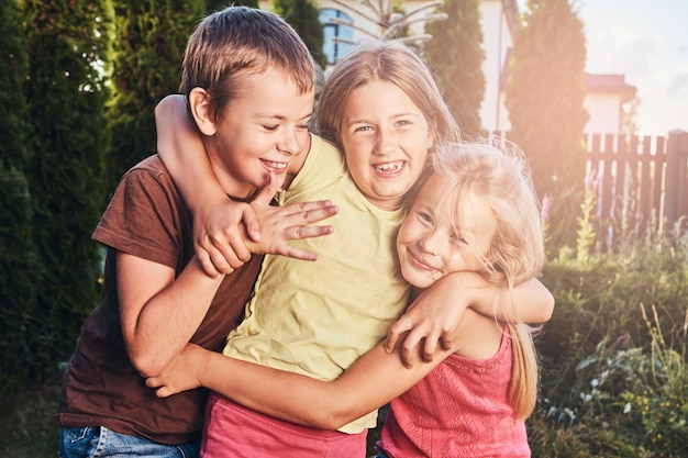Portrait von glücklichen kleinen Freunden, die sich am Hof amüsieren. Drei süße kleine Freunde kuscheln und spielen.