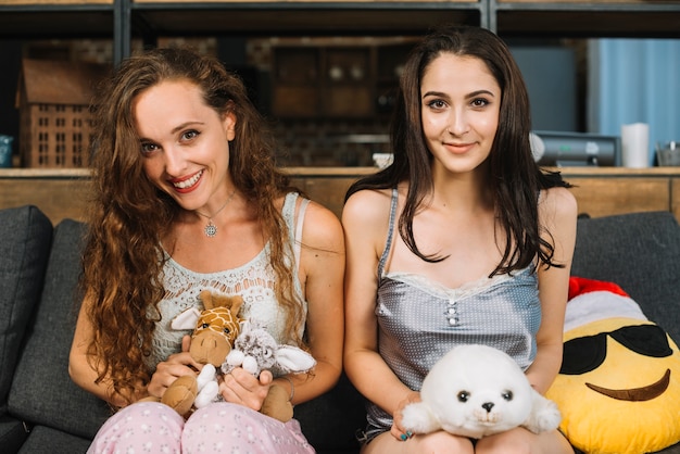 Portrait von zwei jungen Frauen mit dem weichen Spielzeug, das Kamera betrachtet