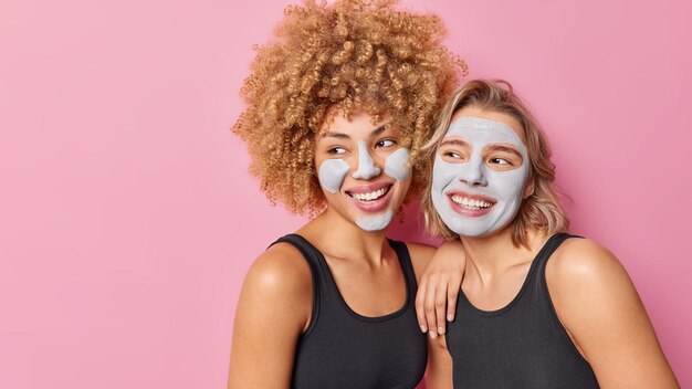 Positiv fröhliche Frauen haben Spaß nebeneinander stehen Schlammmaske auf Gesicht für Hautbehandlung Lächeln gerne isoliert über rosa Hintergrund kopieren Platz für Ihren Text Gesichtspflegekonzept