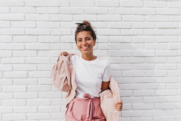 Positiv gebräunte Frau im weißen T-Shirt zieht rosa Jacke an