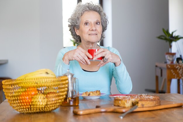 Positive ältere Dame, die geschmackvolle Torte genießt