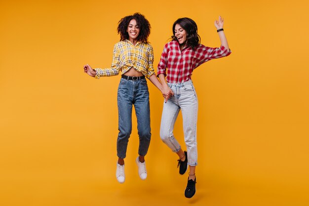 Positive aktive Mädchen mit dunklem gewelltem Haar tanzen. Frauen lachen und genießen Fotoshootings