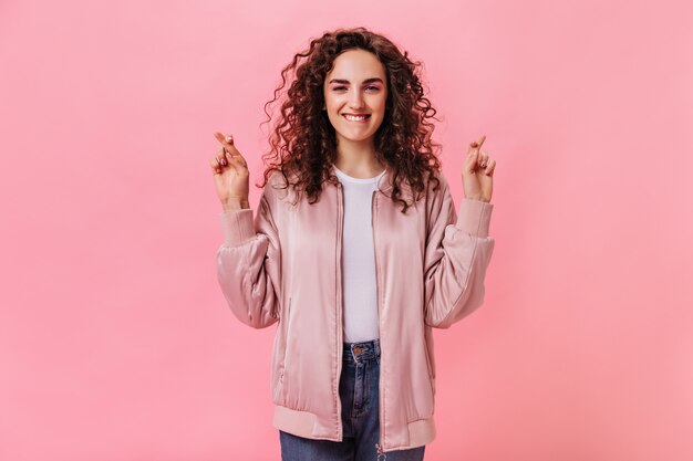 Positive Dame im rosa Outfit kreuzt Finger auf lokalisiertem Hintergrund