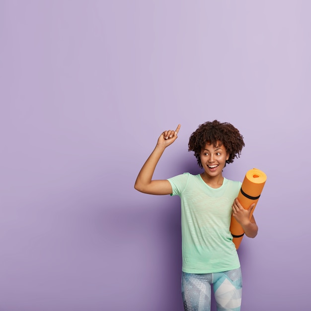 Positive dunkelhäutige Frau mit Afro-Frisur, trägt lässiges T-Shirt und Leggings, hat Fitness-Meditation