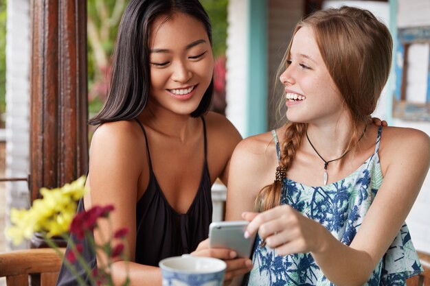 Positive europäische Frauen teilen Eindrücke nach schönen Auslandsferien mit ihrer asiatischen Freundin