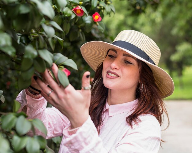 Positive Frau, die das Blumenwachsen auf grünen Zweigen im Park hält