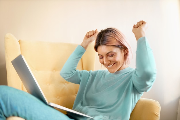 Positive Frau gewinnt einen Preis im Internet und versucht auf dem Stuhl zu tanzen.