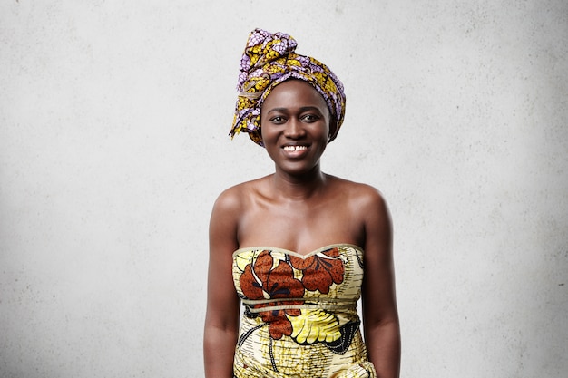 positive fröhliche afrikanische Frau, die schönes buntes Kleid trägt, breit lächelt, ihre weißen Zähne zeigt, sich glücklich und entspannt fühlt, guten Tag genießt. Menschen und Lebensstil