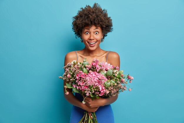 Positive fröhliche entzückende afroamerikanische Frau lächelt breit und hält großen Lieferstrauß von schönen Blumen