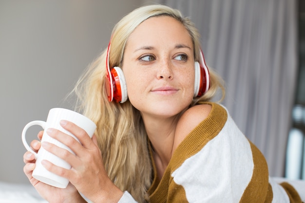 Positive junge Frau in Kopfhörer halten Tasse