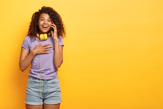 Positive junge Frau mit Afro-Frisur, die gegen die gelbe Wand aufwirft