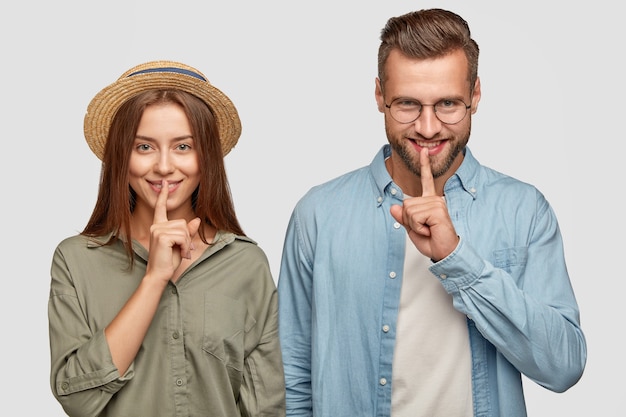 Positive junge Teenager teilen Gerüchte und Klatsch, halten Zeigefinger auf den Lippen