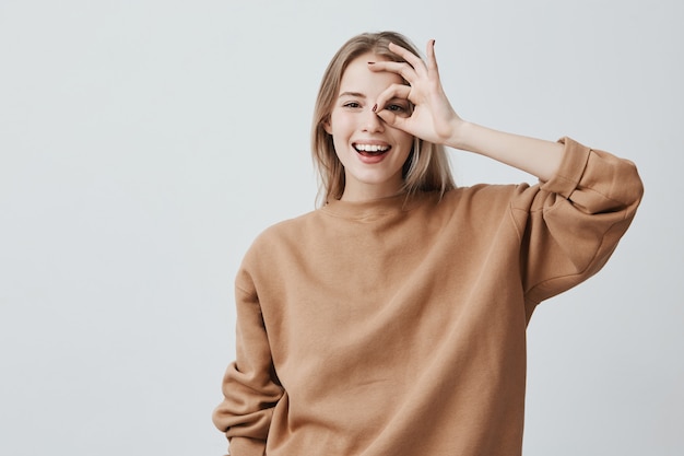 Positive lustige blonde Frau in Freizeitkleidung zeigt ok Zeichen