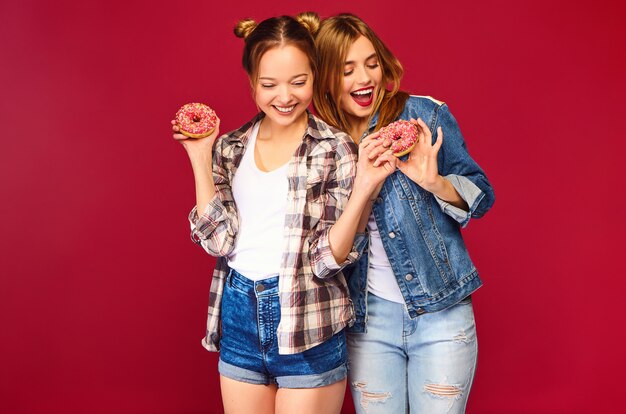 Positive Modelle halten frische rosa Donuts mit Pulver bereit, um Süßigkeiten zu genießen