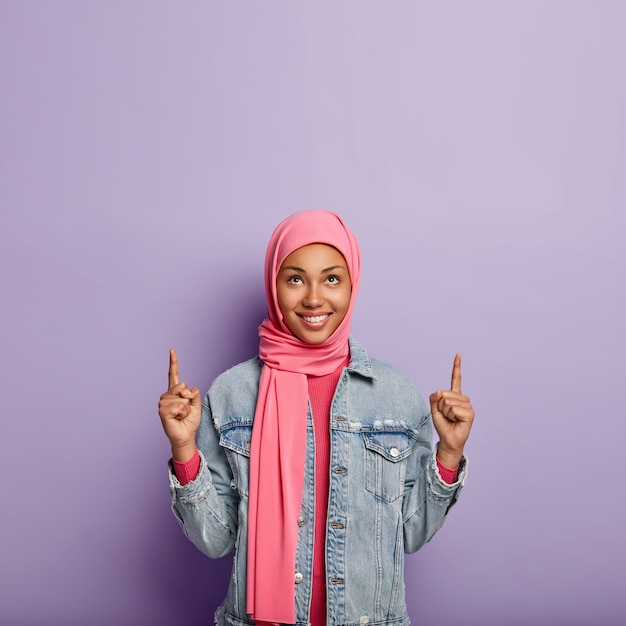 Positive muslimische Dame zeigt oben, diskutiert interessante und glückliche Ereignisse nach oben