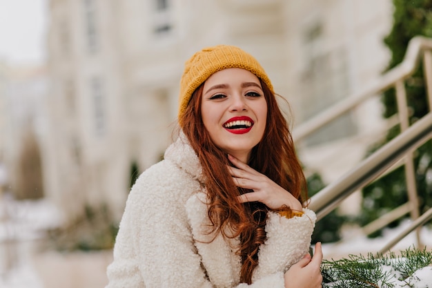 Positive rothaarige Frau, die über verschwommene Natur lacht. Raffiniertes Ingwermädchen, das während des Winterfotoshootings lächelt.