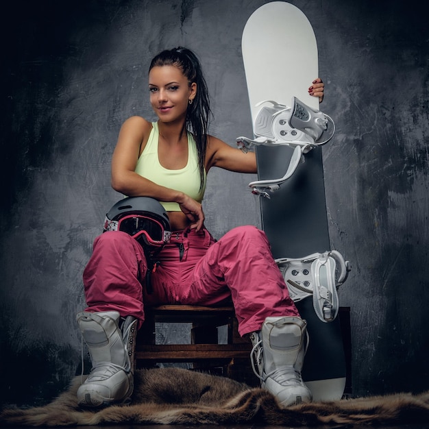 Positive sonnengebräunte sportliche Frau posiert mit Snowboard in einem Studio.