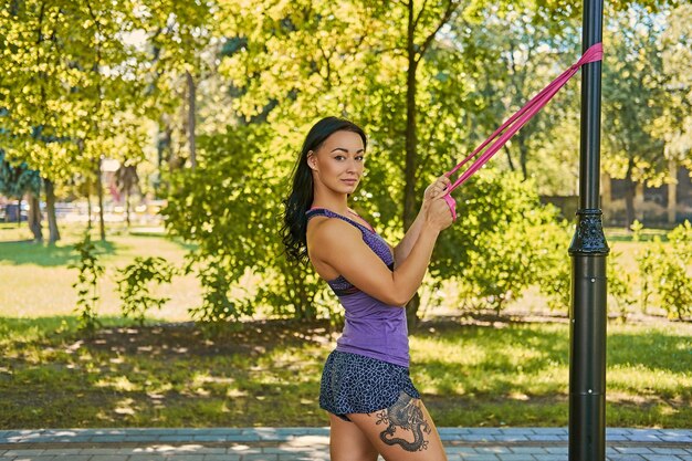 Positive sportliche Frau, die mit Trx-Streifen in einem Herbstpark trainiert.