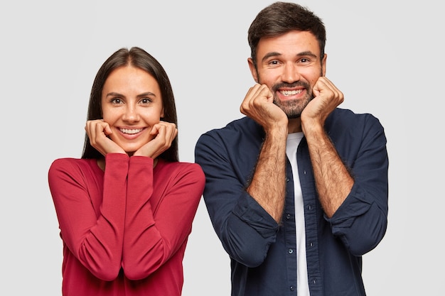 Positive Teenager halten die Hände unter dem Kinn und lächeln zahnig warm