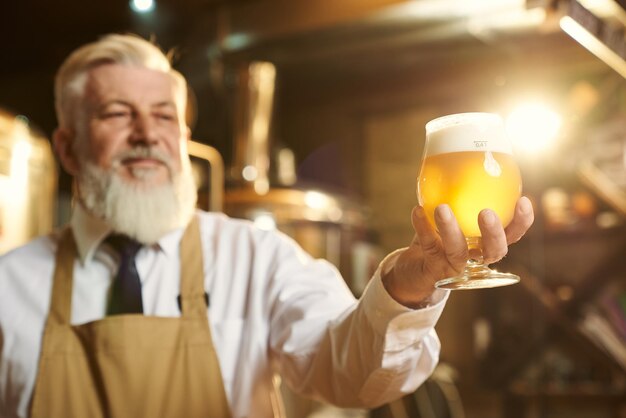 Positiver Brauer, der Bierglas mit Schaum hält