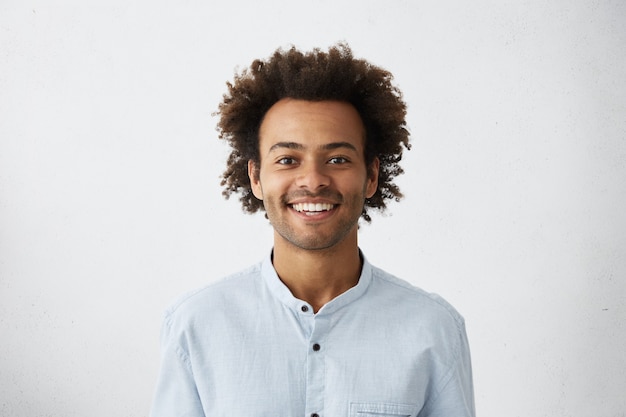 Positiver Kerl mit afrikanischer Frisur und dunkler Haut, die elegantes weißes Hemd trägt