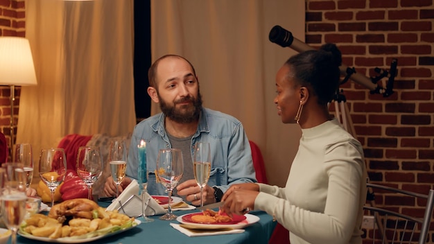 Positiver mann, der mit verwandten spricht, während er das weihnachtsessen zu hause genießt. festliche, glückliche familienmitglieder versammelten sich im wohnzimmer, um gemeinsam das traditionelle winterfest beim essen und trinken zu feiern.