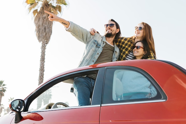 Positiver Mann, der nahe den lächelnden Frauen sich heraus lehnt vom Auto zeigt