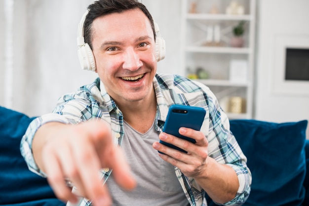 Positiver Mann mit hörender Musik des Smartphone in den Kopfhörern auf Sofa