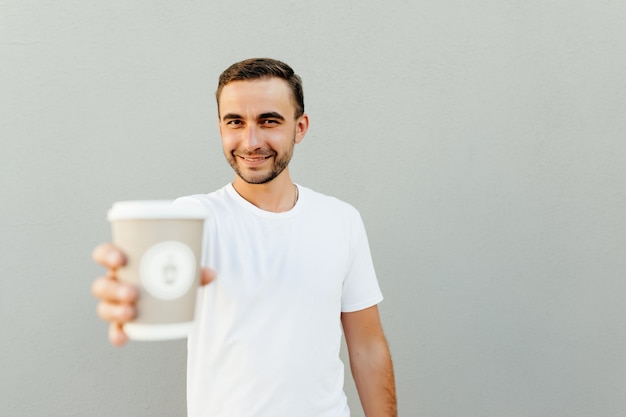 Positiver Mann wies Pappbecher Kaffee isoliert über grauer Wand