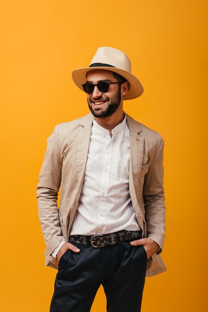 Positiver Typ mit Hut und Sonnenbrille, der auf isoliertem Hintergrund lächelt