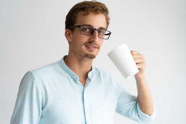 Positiver überzeugter trinkender Kaffee des Mannes und Betrachten der Kamera.