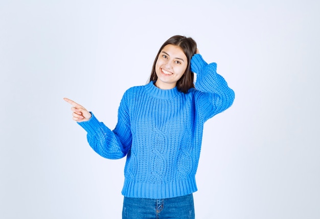 Positives Brunettemädchen in der blauen Strickjacke, die auf Weiß steht.