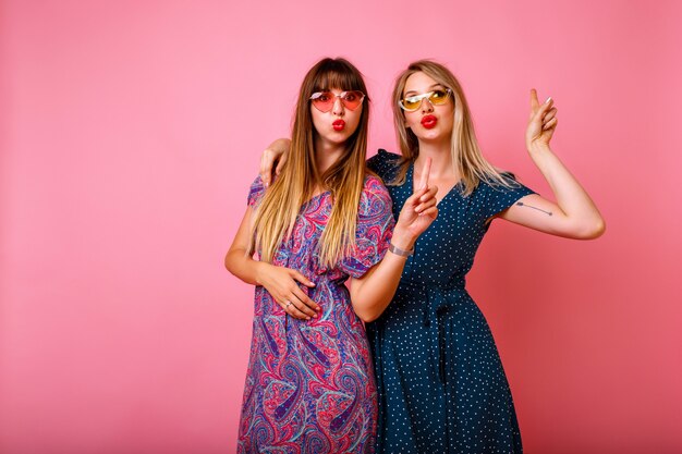 Positives Porträt der besten Freunde Hipster Schwester Mädchen Umarmungen lächelnd und Luftküsse machen, Freundschaftsbeziehungen, für immer zusammen, rosa Wand, trendige Sommeroutfits.