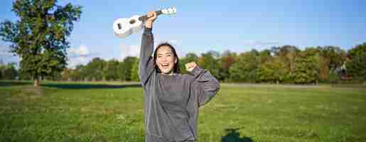 Kostenloses Foto positives schönheitsmädchen mit ukulele tanzt und fühlt sich frei, sieht aufgeregt, triumphiert und