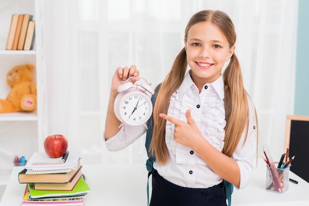 Positives Schulmädchen, das auf Uhr zeigt