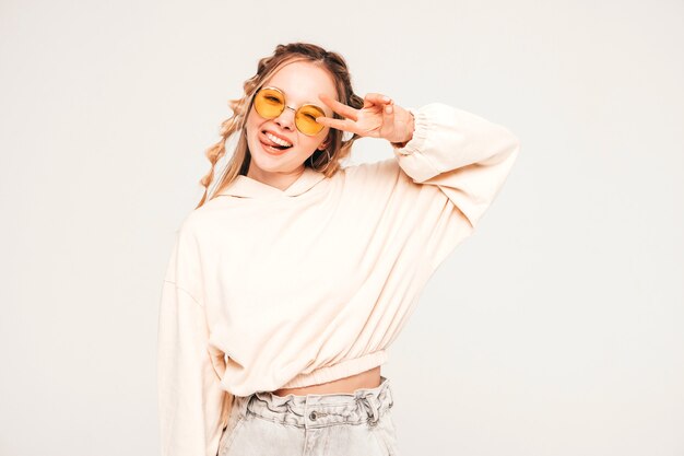 Positives und lustiges Model posiert auf grauer Wand im Studio mit Sonnenbrille