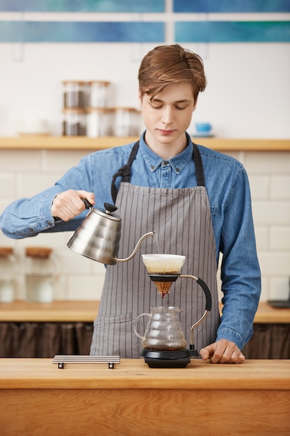 Pouron Kaffee machen. Netter Barista, der Kaffeegetränk bereitet und konzentriert aussieht.